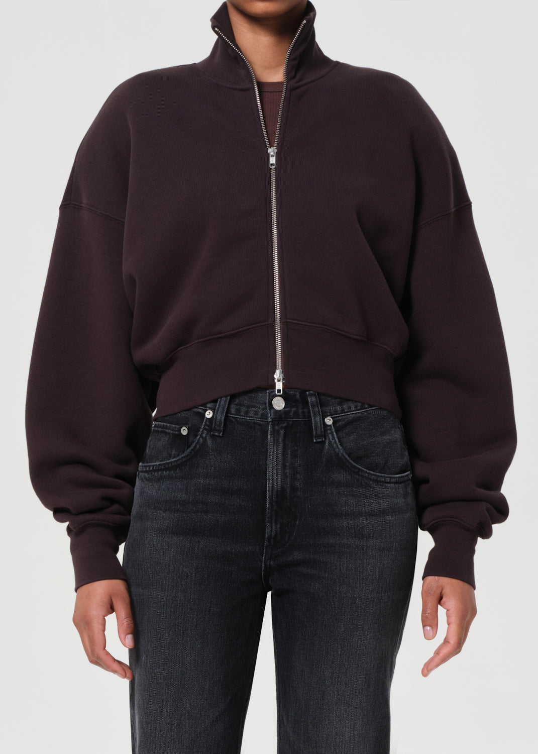 Person wearing a dark brown zip-up sweatshirt and black jeans on a white background