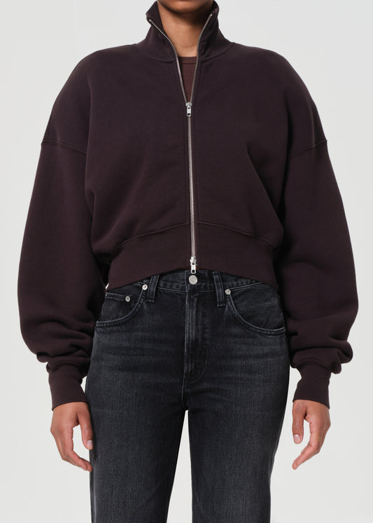 Person wearing a dark brown zip-up sweatshirt and black jeans on a white background