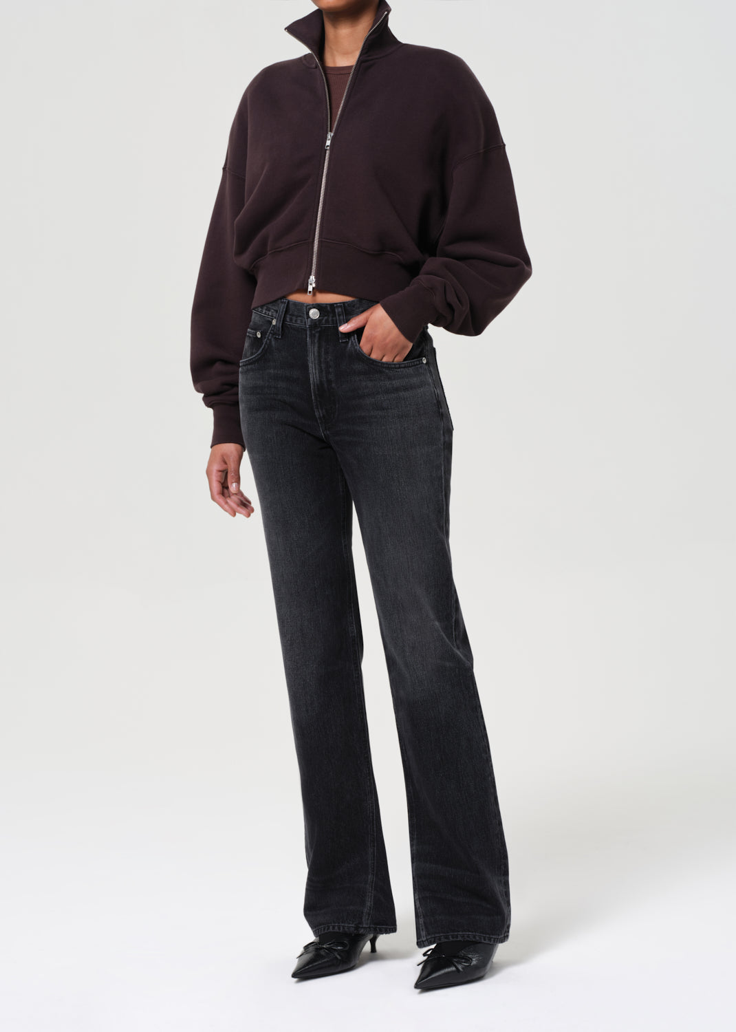 Person wearing a dark brown zip-up sweater and black jeans on a white background