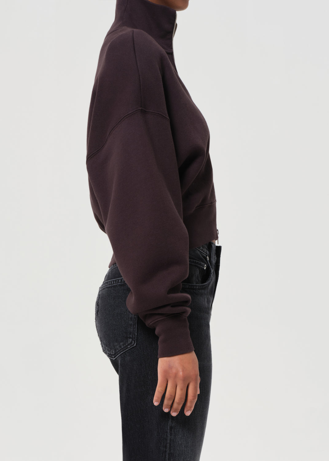 Person wearing a dark brown oversized sweater and black jeans on a white background