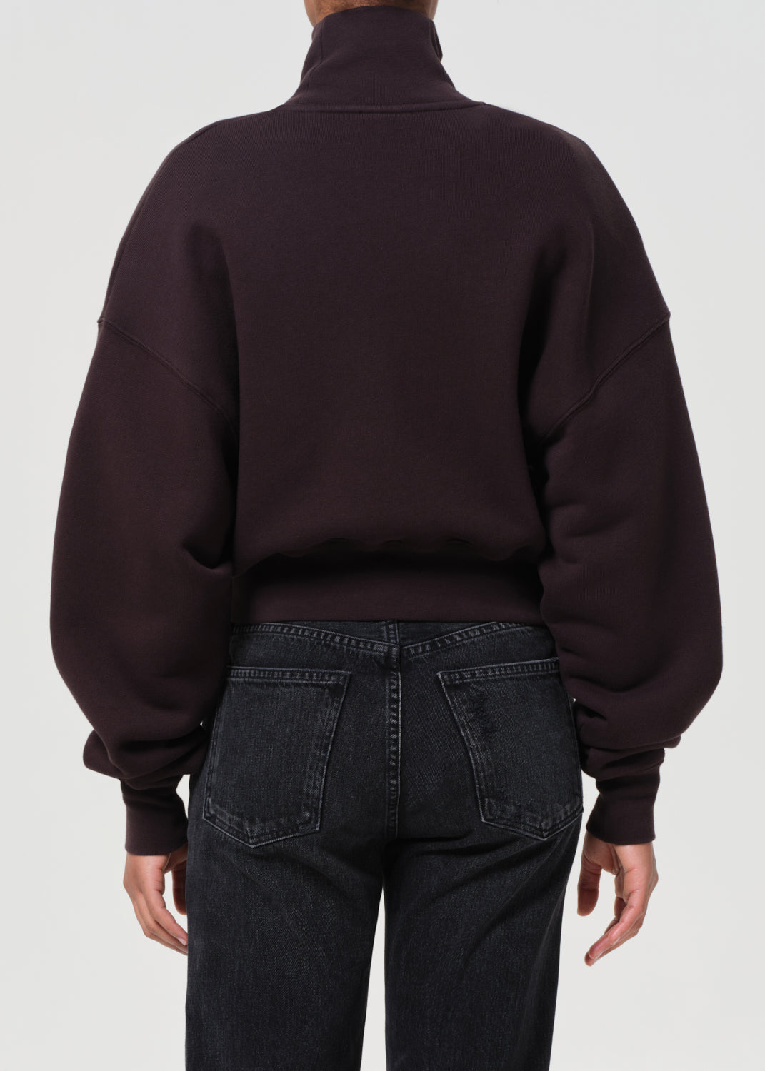 Person wearing a dark brown oversized sweater and black jeans on a white background