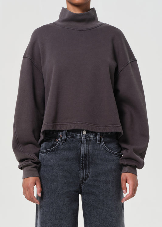Person wearing a dark brown cropped sweatshirt and jeans on a light gray background