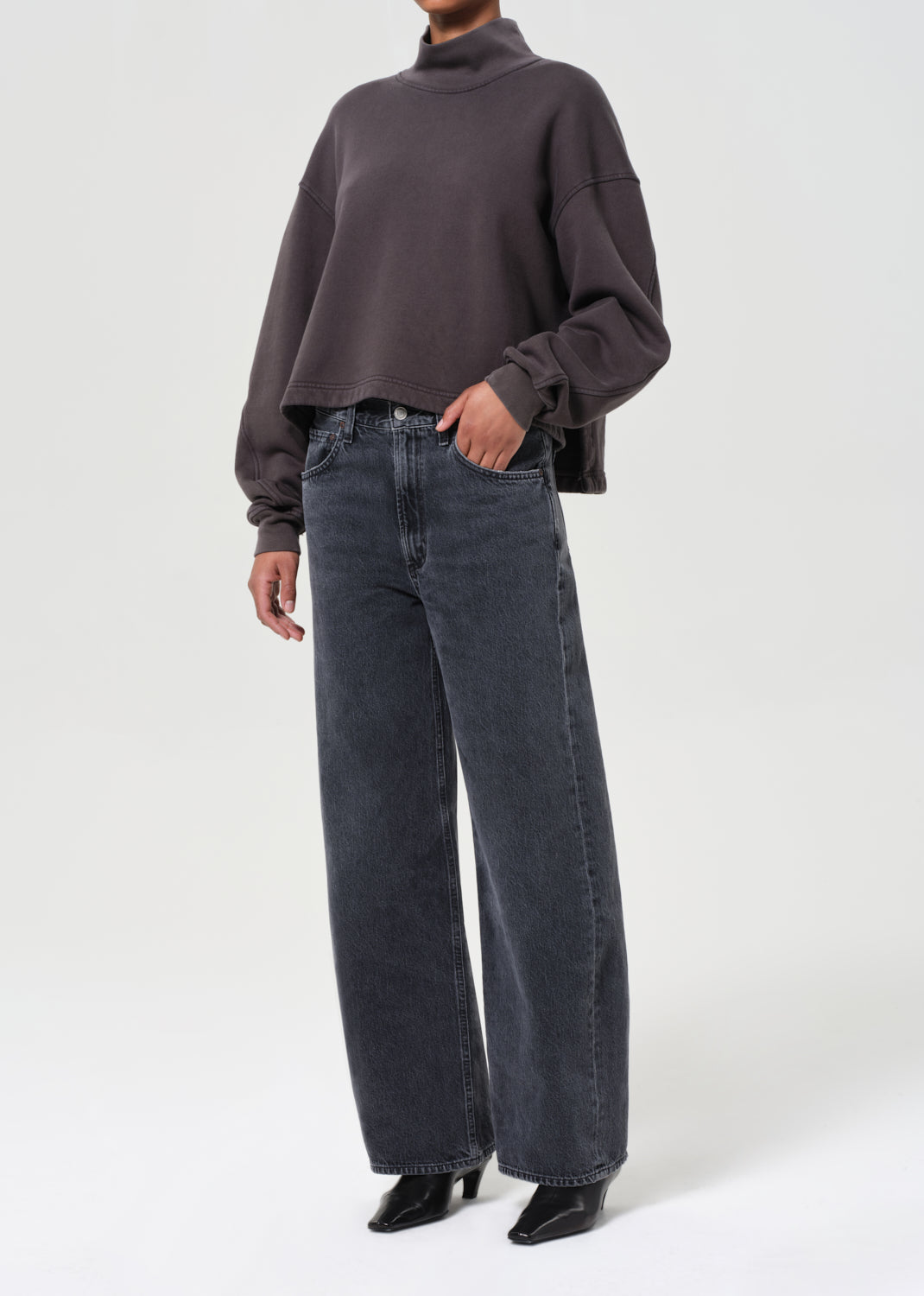Person wearing a dark gray sweater and blue jeans on a white background