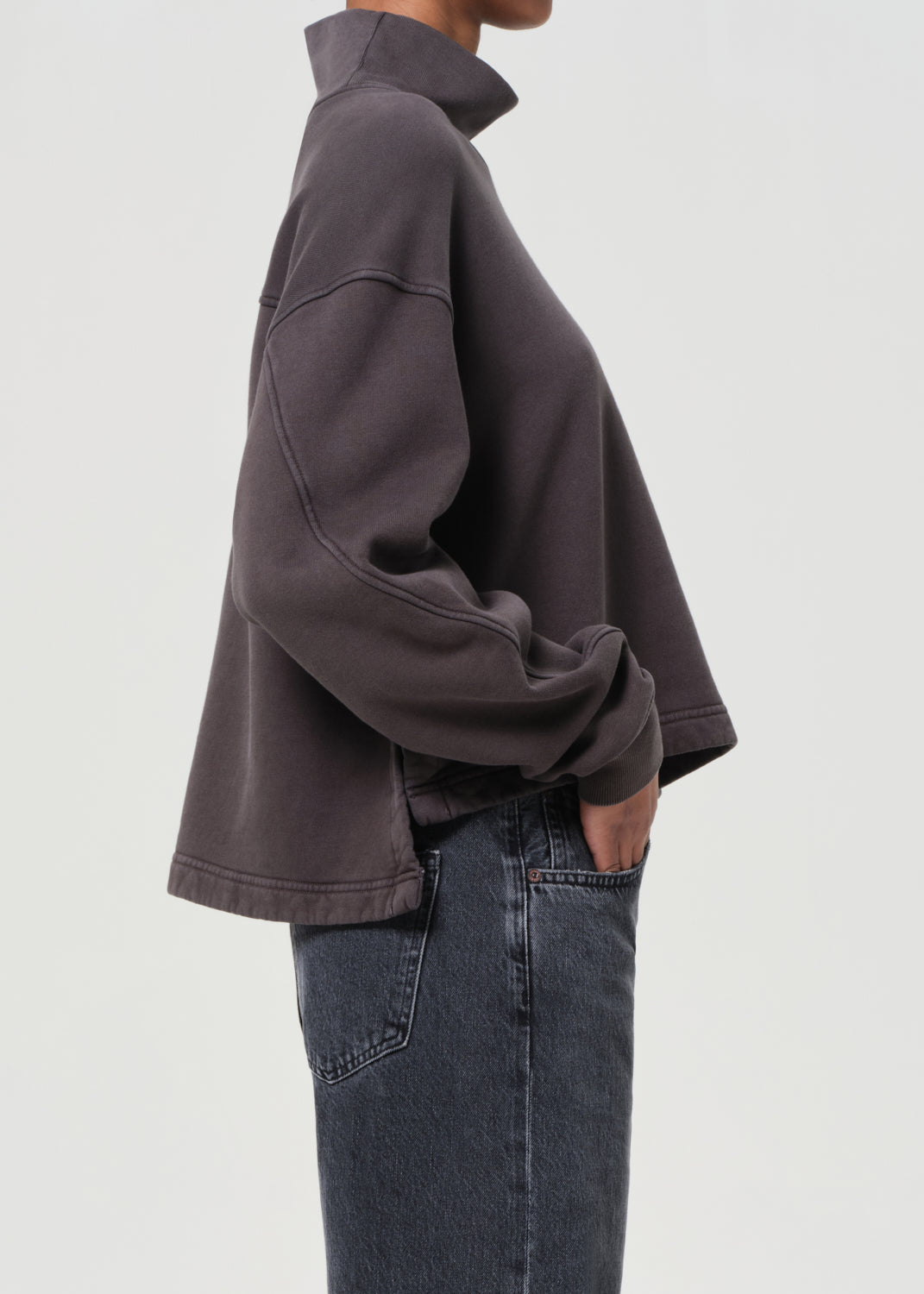 Person wearing a dark gray jacket and jeans on a light gray background