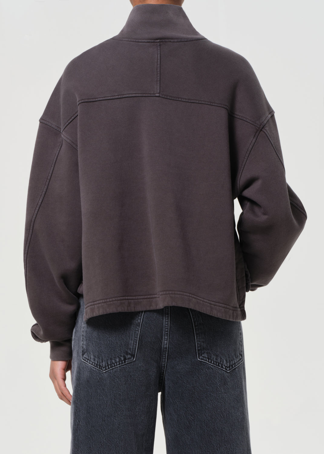 Person wearing a dark brown jacket and jeans on a white background