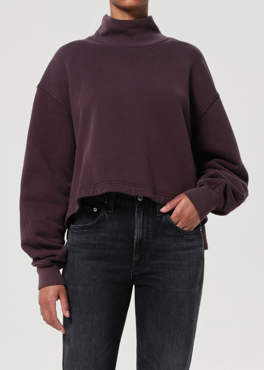 Person wearing a dark purple cropped sweatshirt and black jeans on a light gray background