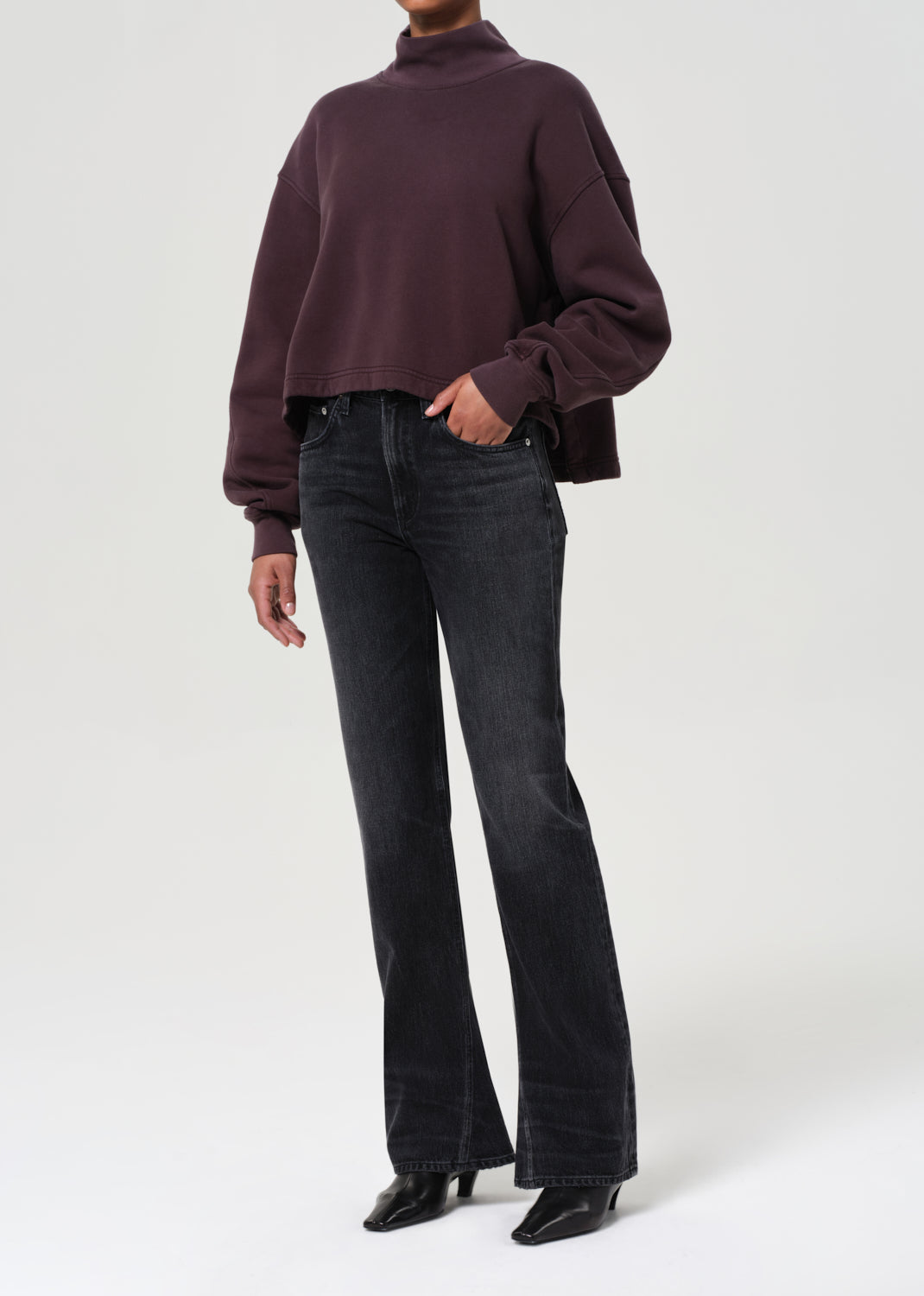 Person wearing a dark brown sweater and black jeans on a white background