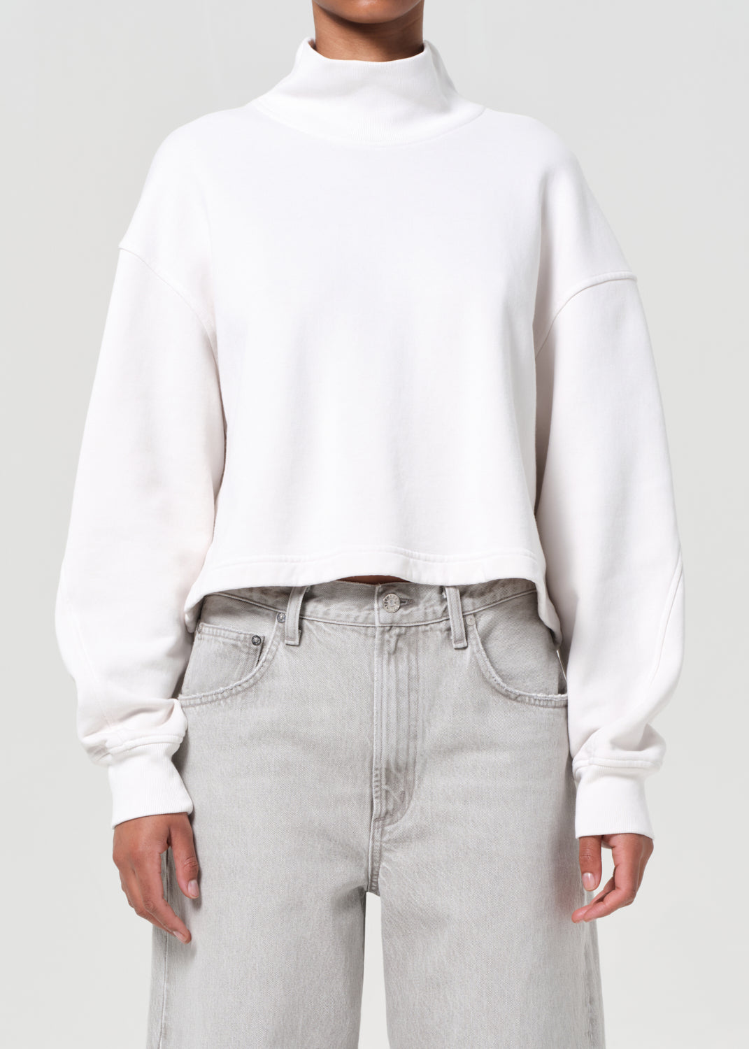 Person wearing a white sweater and light gray jeans on a plain background