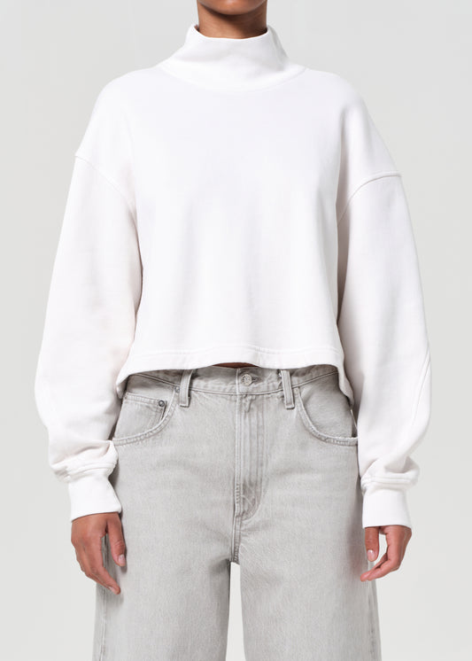 Person wearing a white sweater and light gray jeans on a plain background