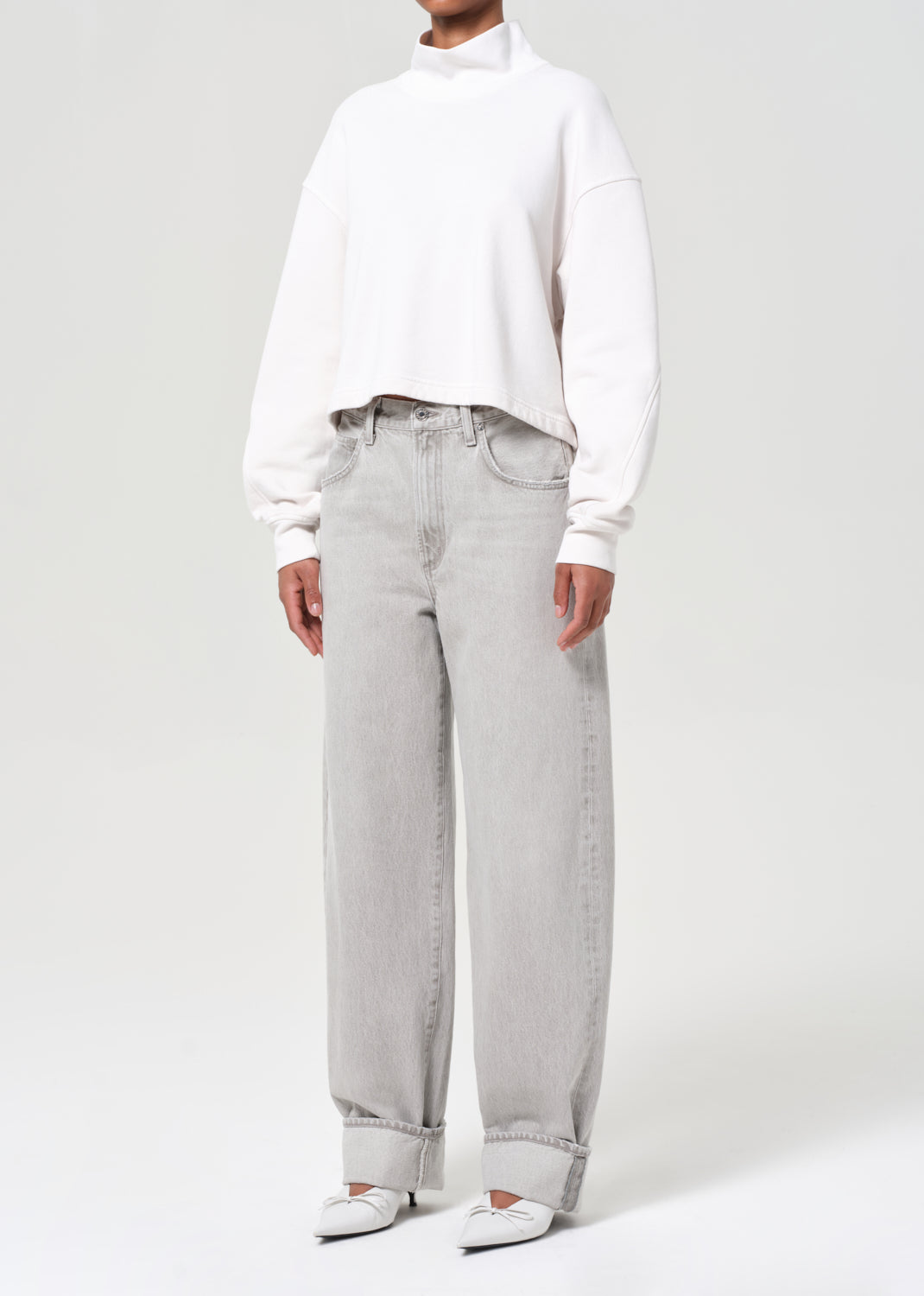 Person wearing a white sweater and light gray jeans on a white background