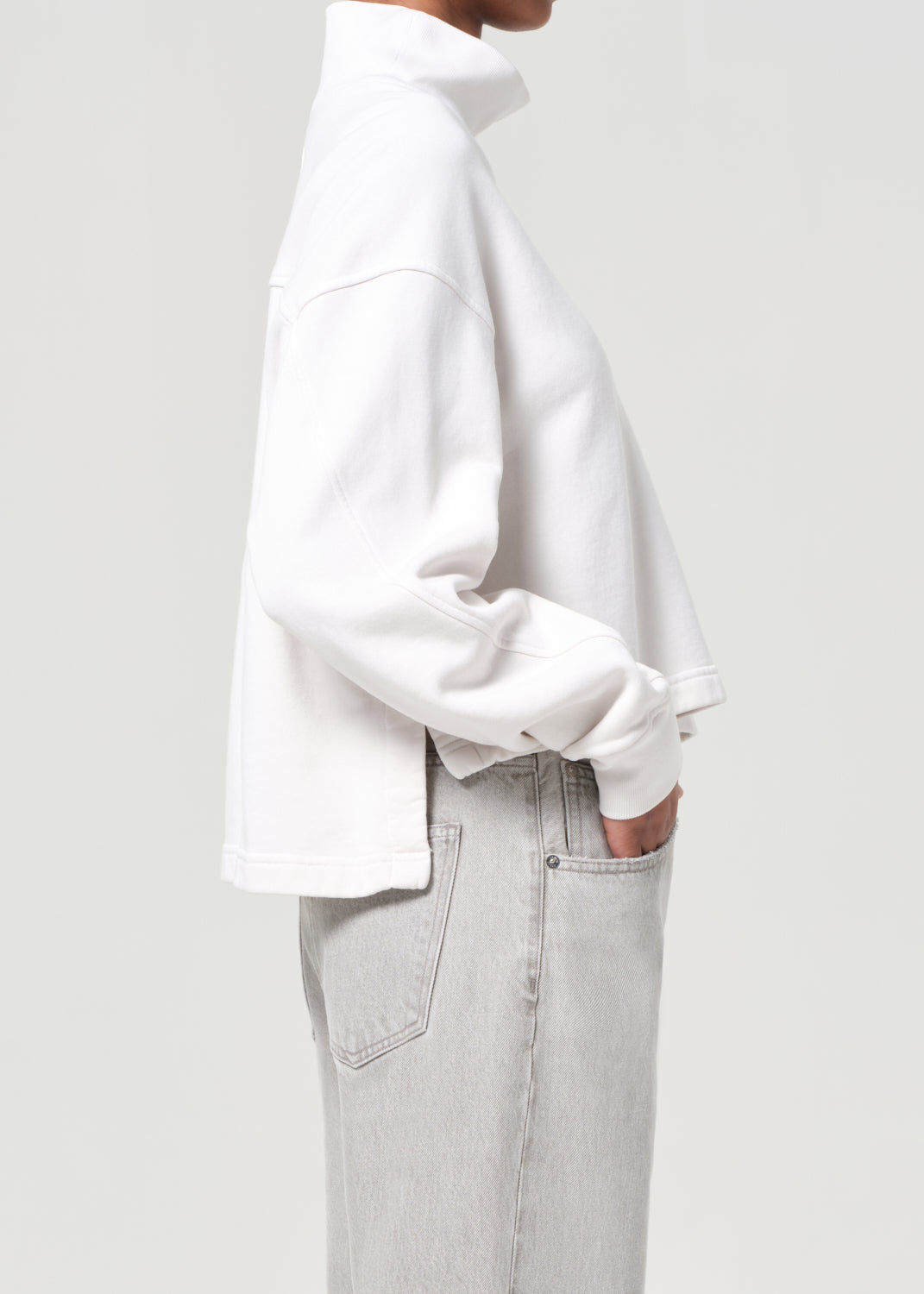 Person wearing a white oversized shirt and light gray pants on a plain background