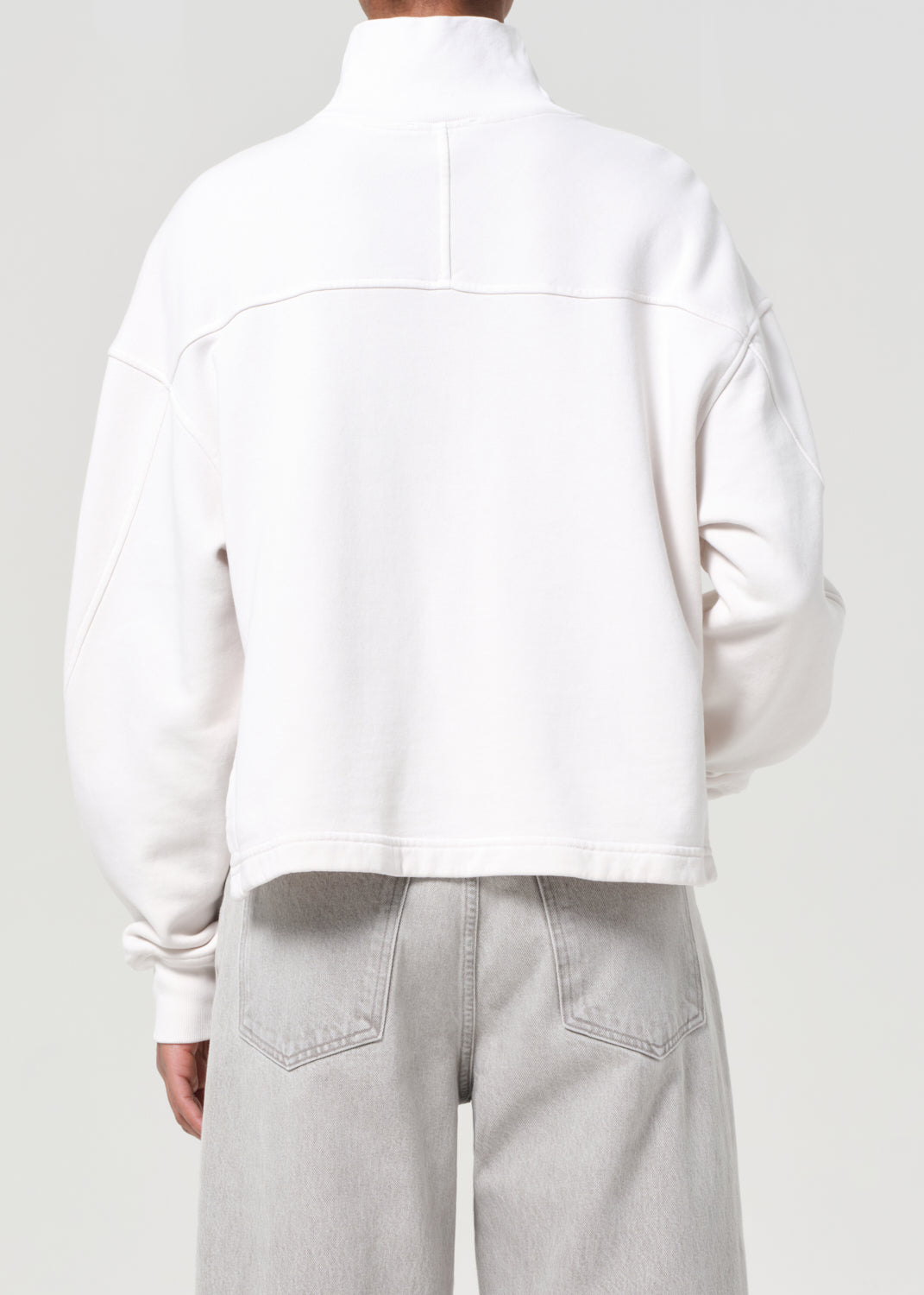 Person wearing a white jacket and light gray pants on a plain background