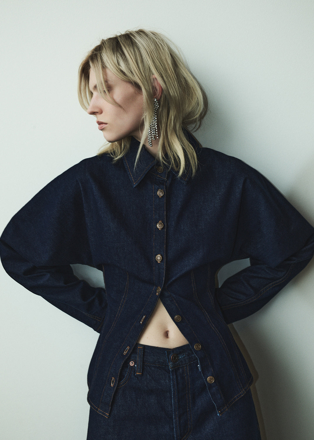 Person wearing a dark denim jacket and pants against a plain background