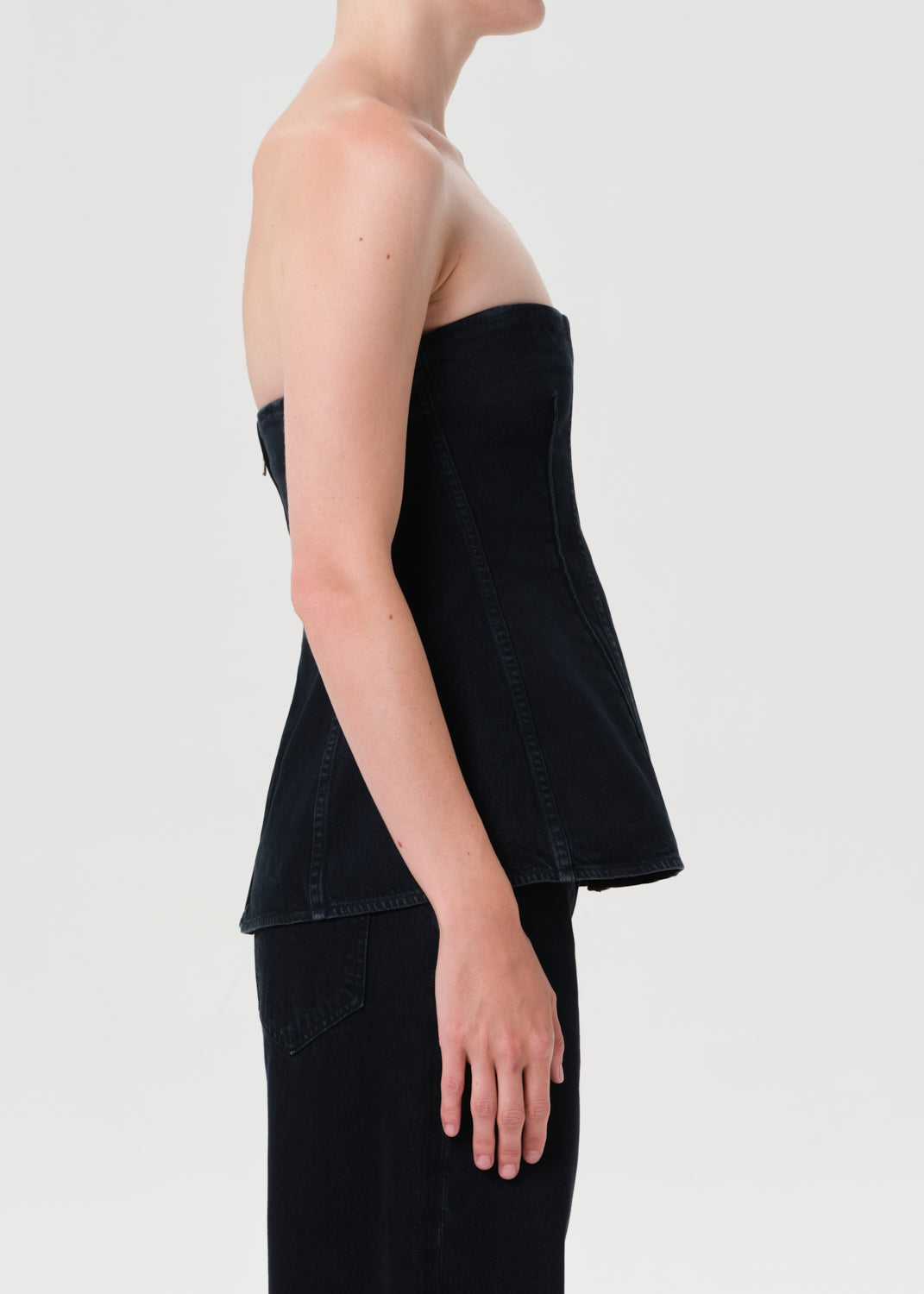 Person wearing a black strapless top and black pants on a light gray background