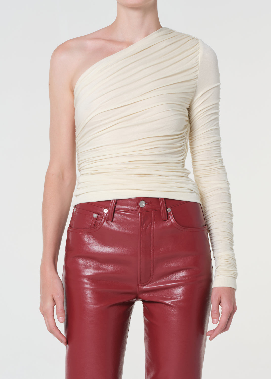 Person wearing a cream one-shoulder top and red leather pants on a white background