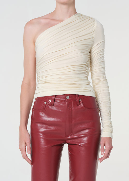 Person wearing a cream one-shoulder top and red leather pants on a white background