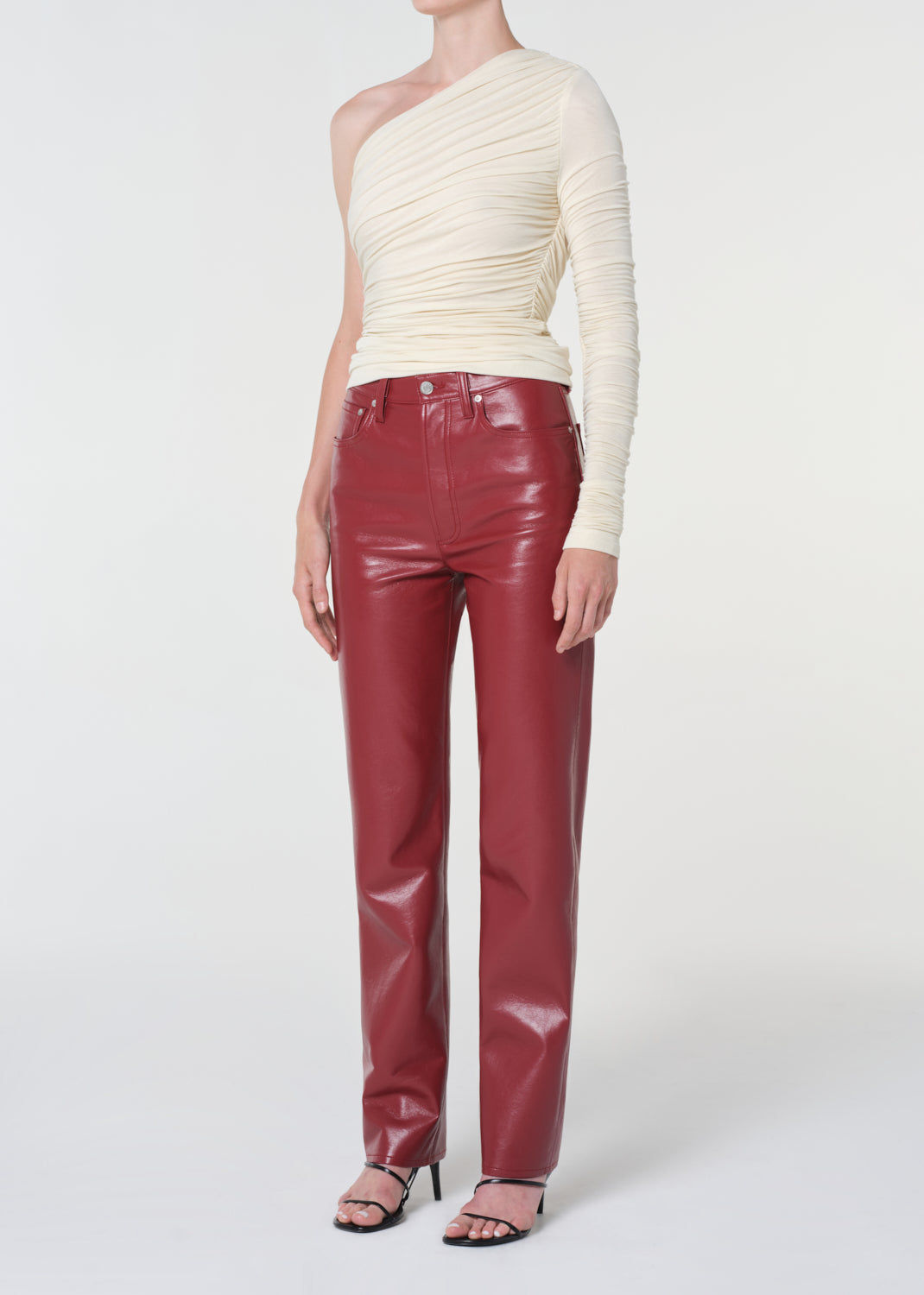 Person wearing a cream one-shoulder top and red shiny pants on a white background
