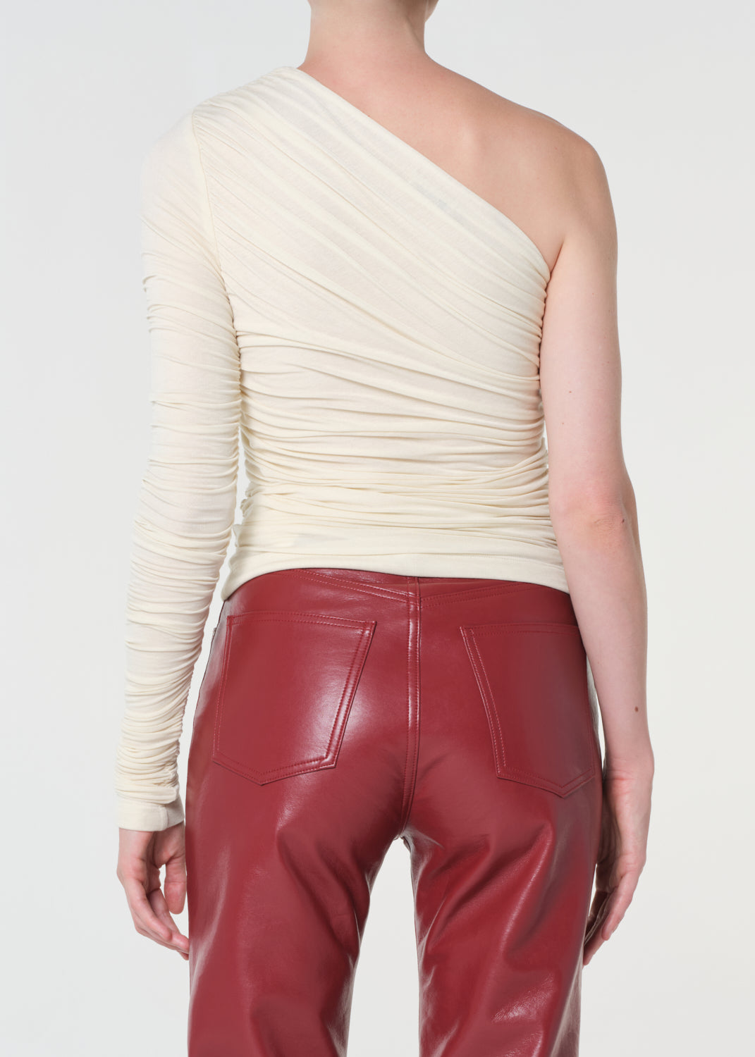 Person wearing a cream one-shoulder top and red leather pants on a white background