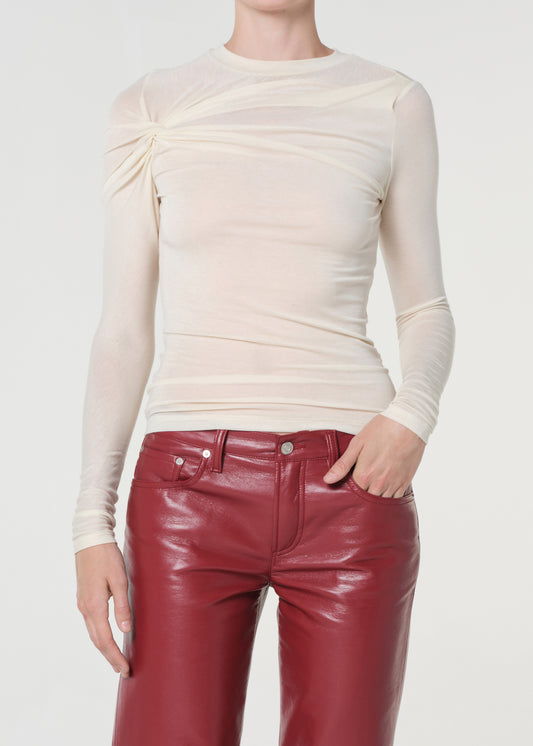 Person wearing a cream long-sleeve top and red leather pants on a white background
