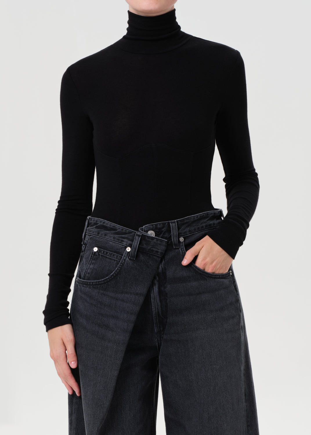 Person wearing a black turtleneck and dark jeans on a light gray background