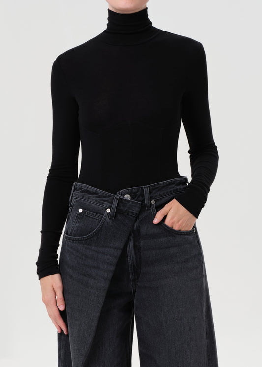 Person wearing a black turtleneck and dark jeans on a light gray background