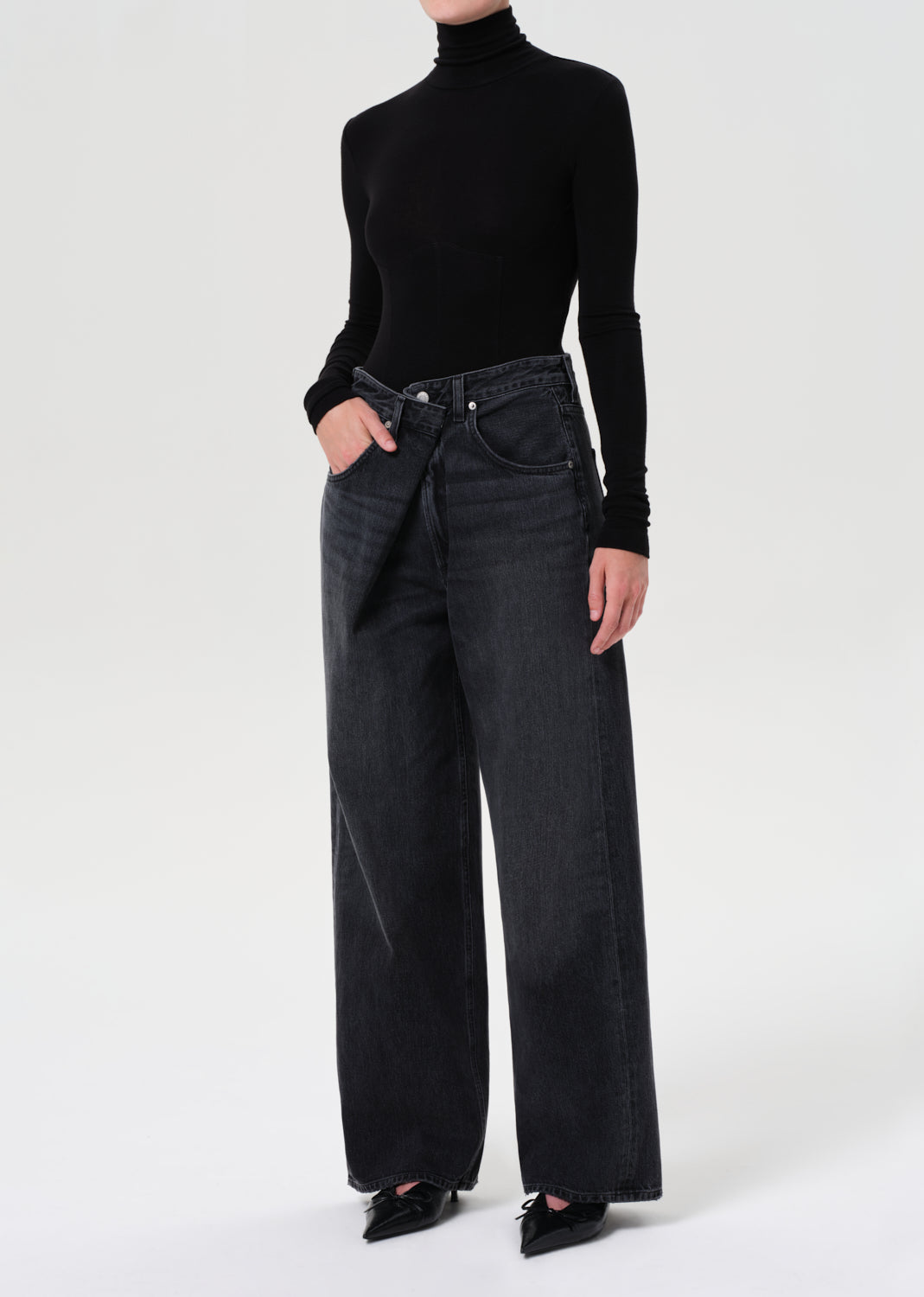Person wearing a black turtleneck and wide-leg jeans on a white background