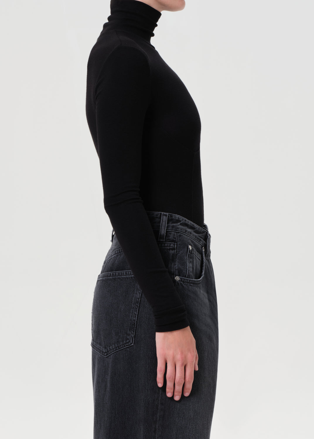 Person wearing a black turtleneck and dark jeans on a light gray background