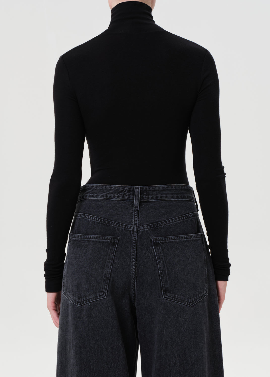 Person wearing a black turtleneck and dark jeans on a white background