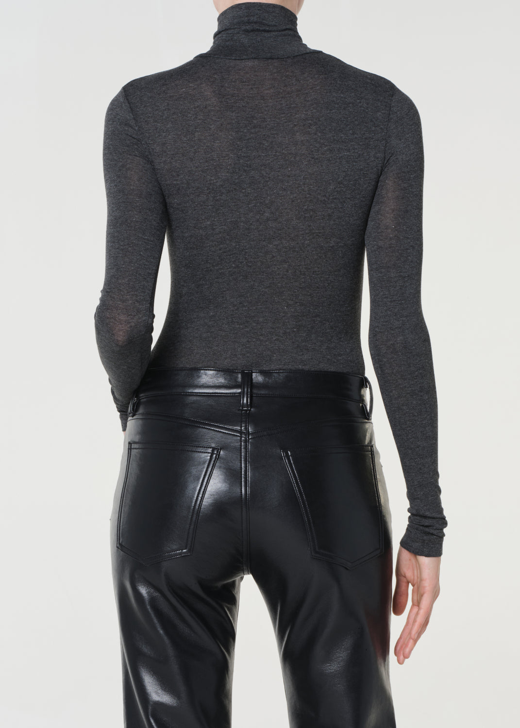 Person wearing a dark gray turtleneck sweater and black leather pants on a white background