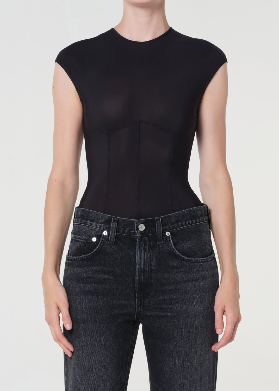 Person wearing a black sleeveless top and dark jeans on a white background