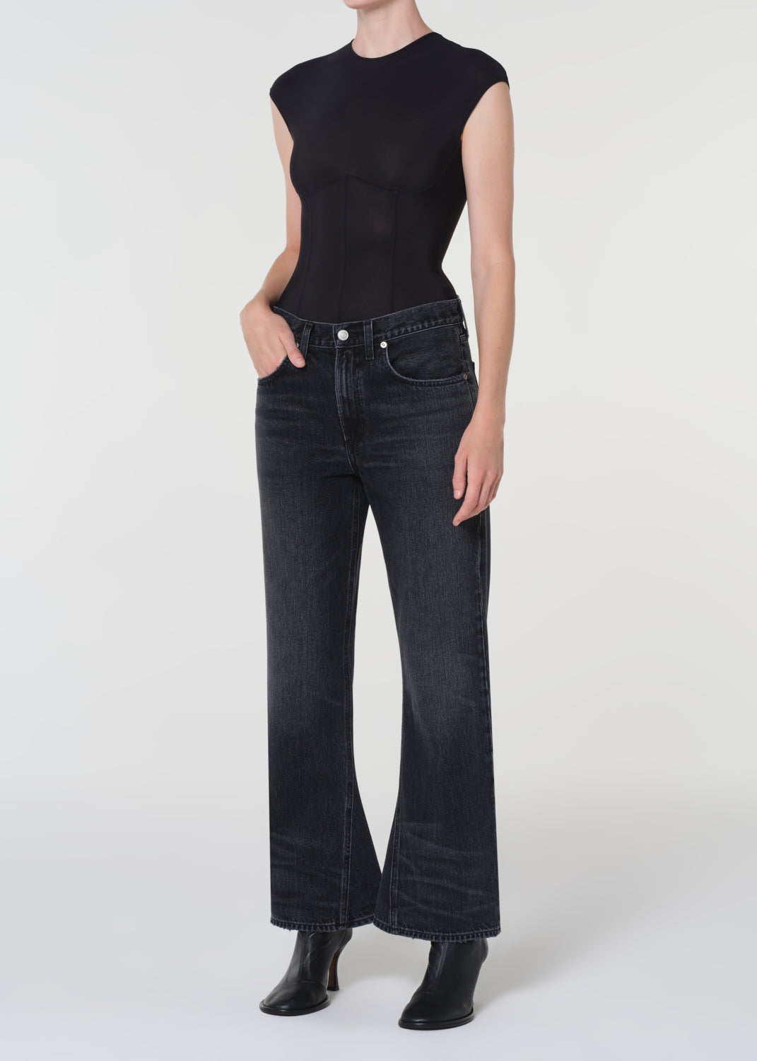 Person wearing a black sleeveless top and dark jeans on a white background