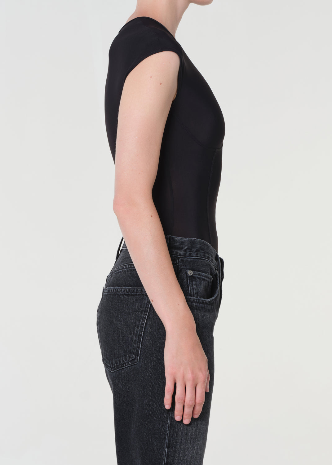 Person wearing a black sleeveless top and dark jeans on a light gray background