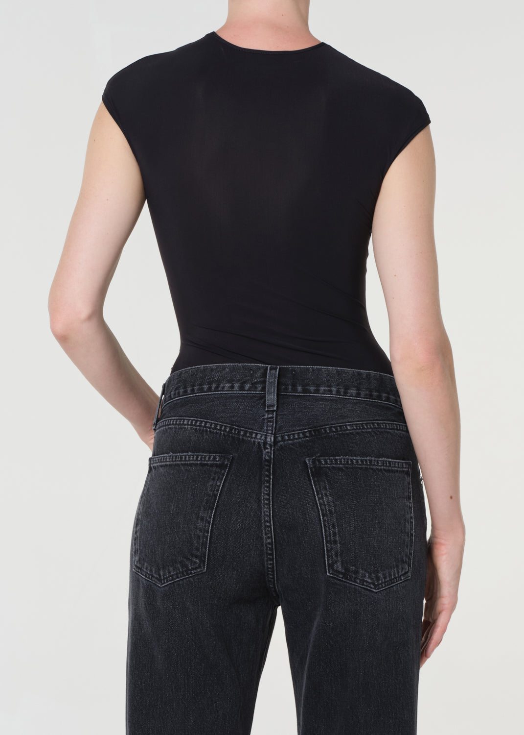 Person wearing a black sleeveless top and black jeans on a white background
