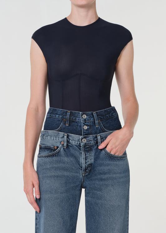 Person wearing a black sleeveless top and blue jeans on a white background