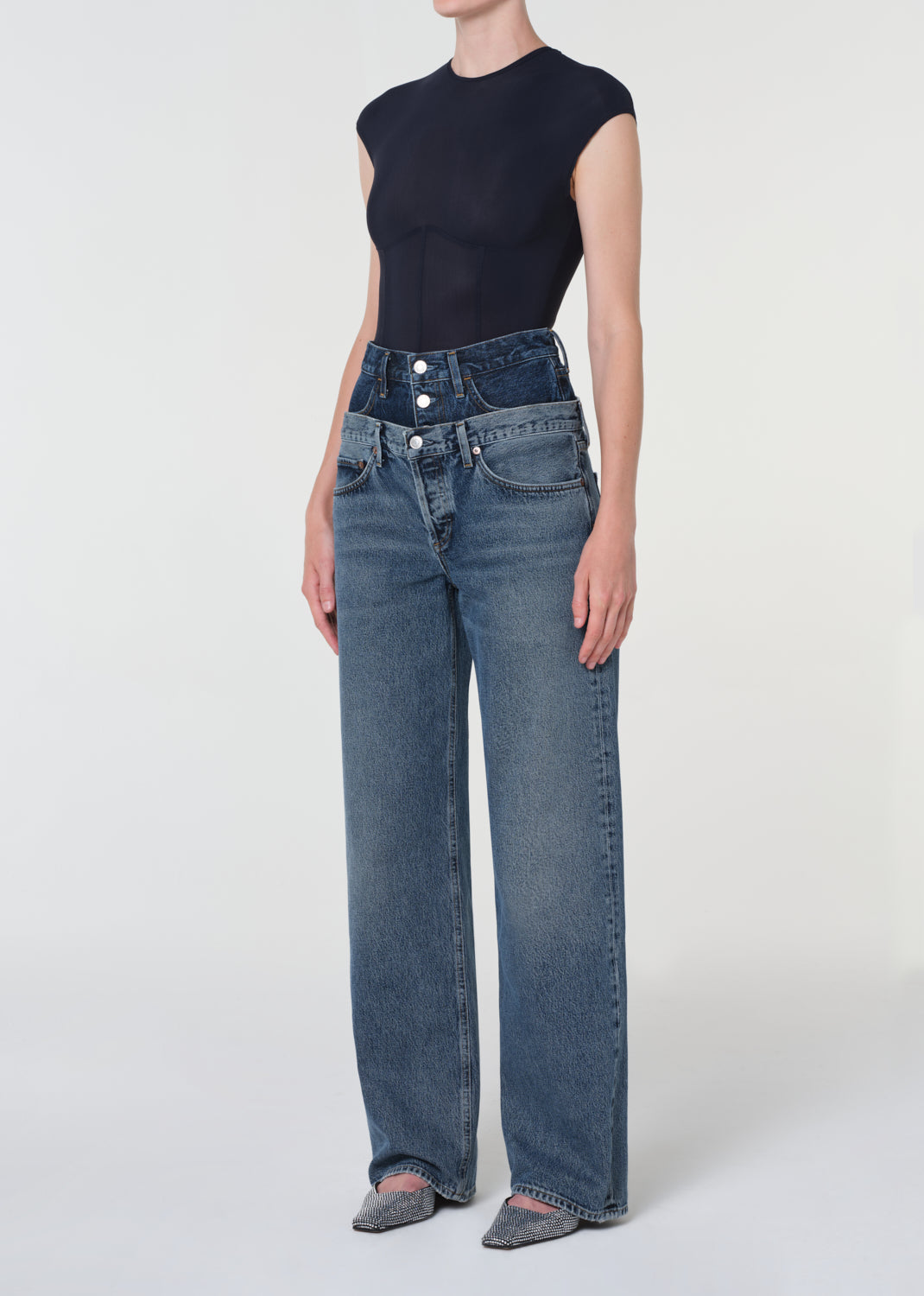 Person wearing a black sleeveless top and blue jeans on a white background