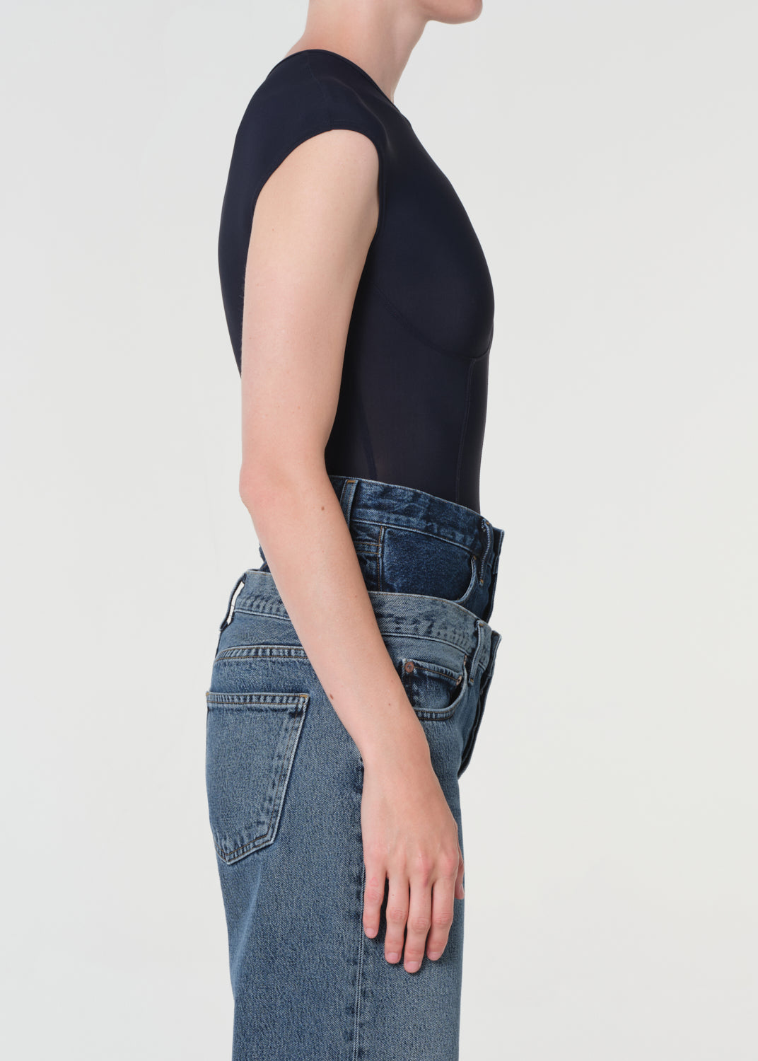Person wearing a black t-shirt and blue jeans on a light gray background