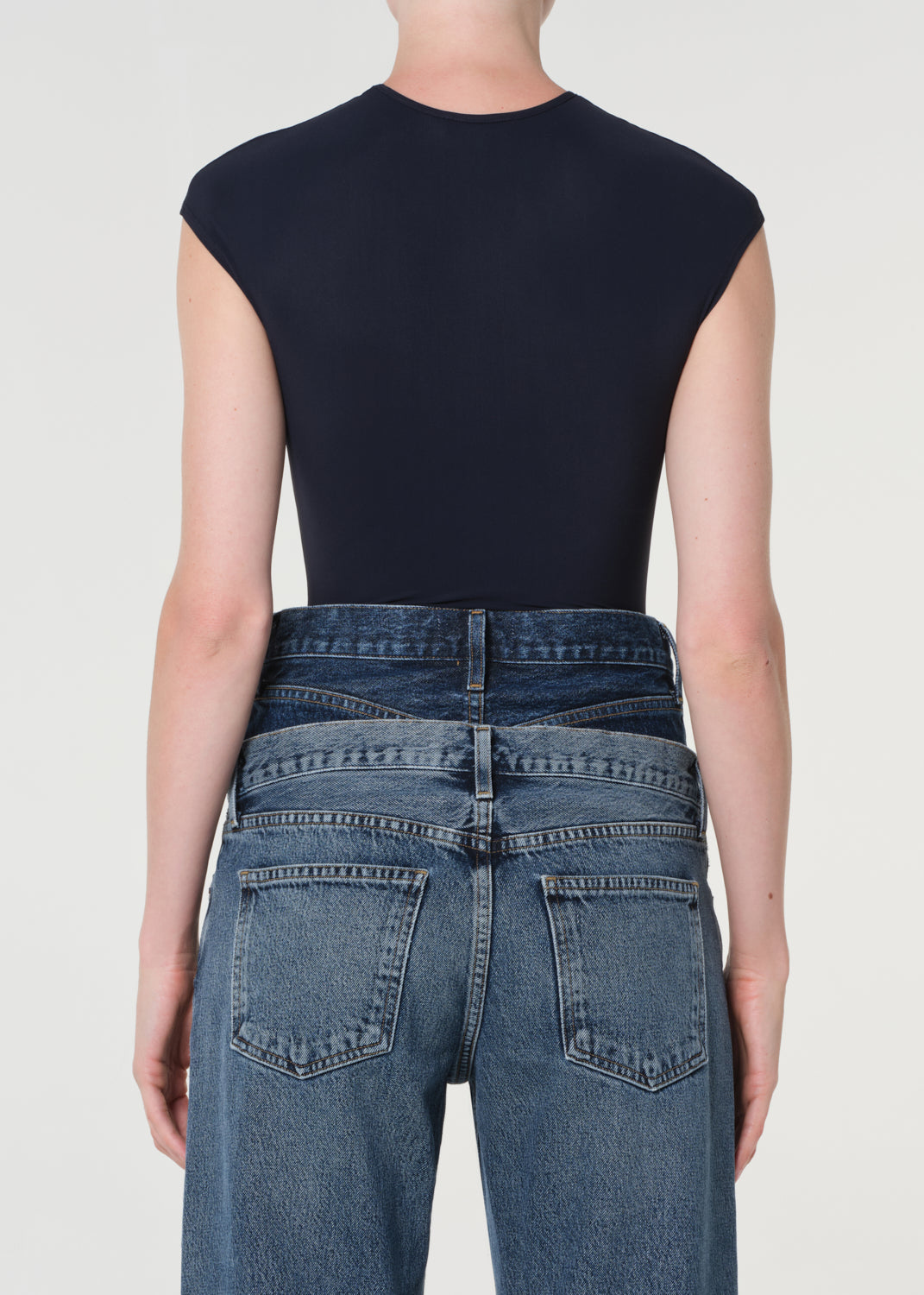 Person wearing a black sleeveless top and blue jeans on a white background