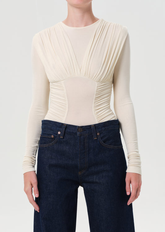 Person wearing a cream ribbed long-sleeve top and dark blue jeans on a white background