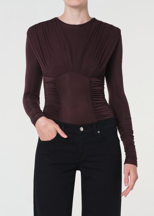 Person wearing a brown long-sleeve top with a ruched design on a white background