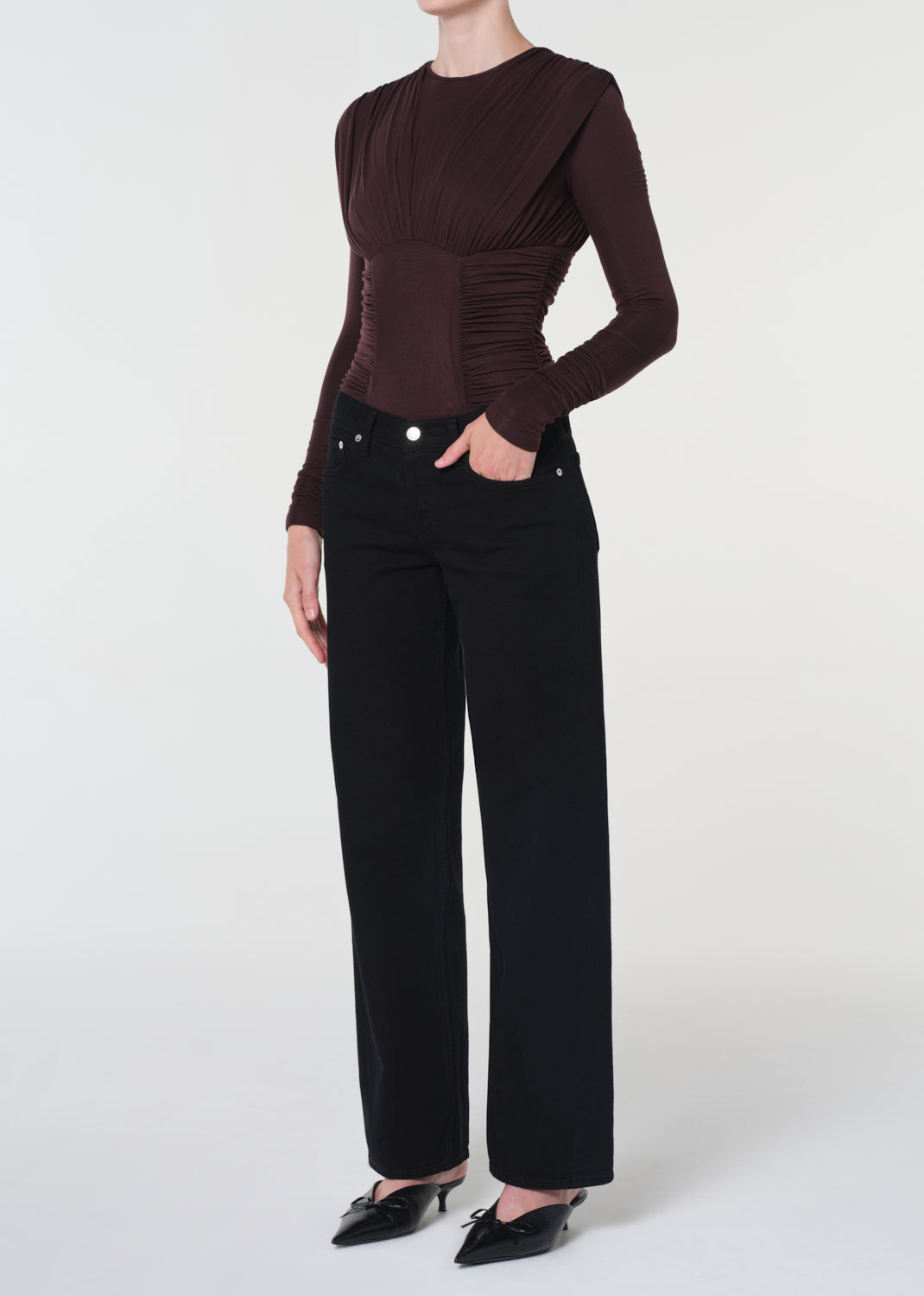 Person wearing a brown long-sleeve top and black pants on a white background