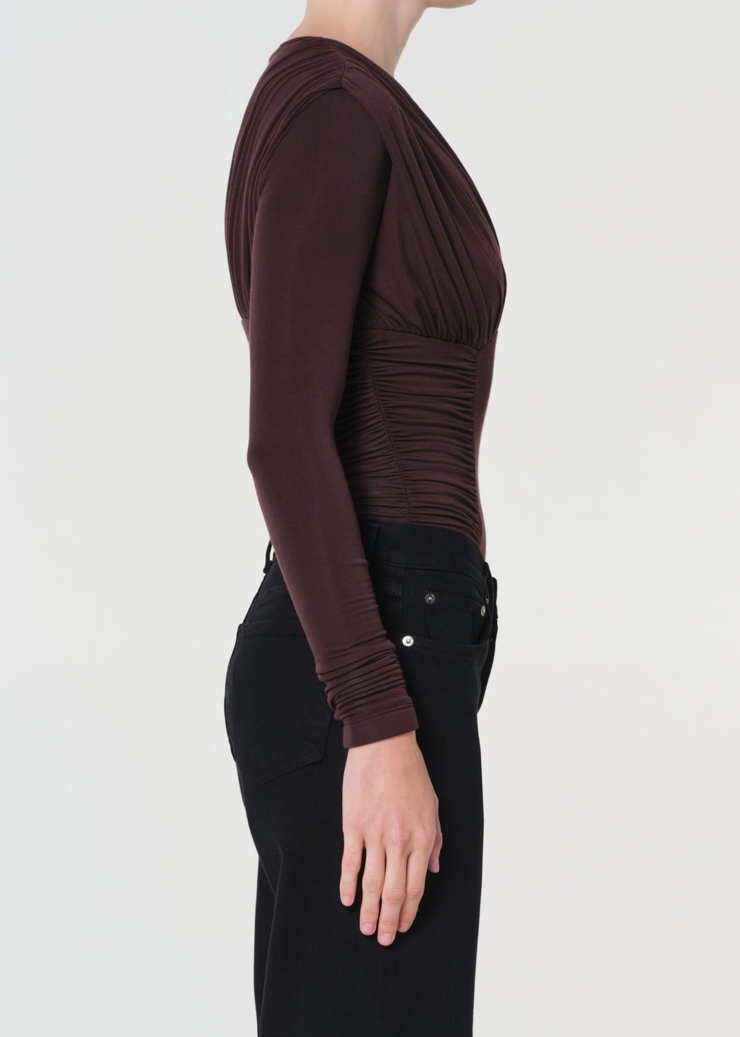 Person wearing a dark brown long-sleeve top and black pants on a light gray background