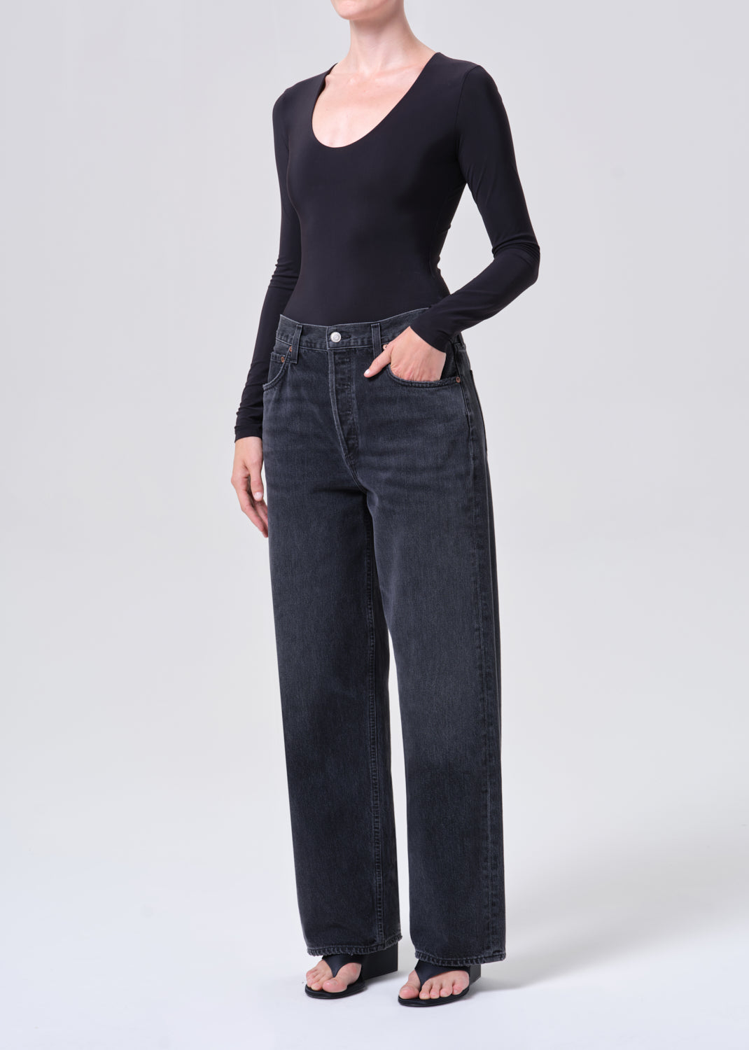 Person wearing a black long-sleeve top and dark jeans on a white background