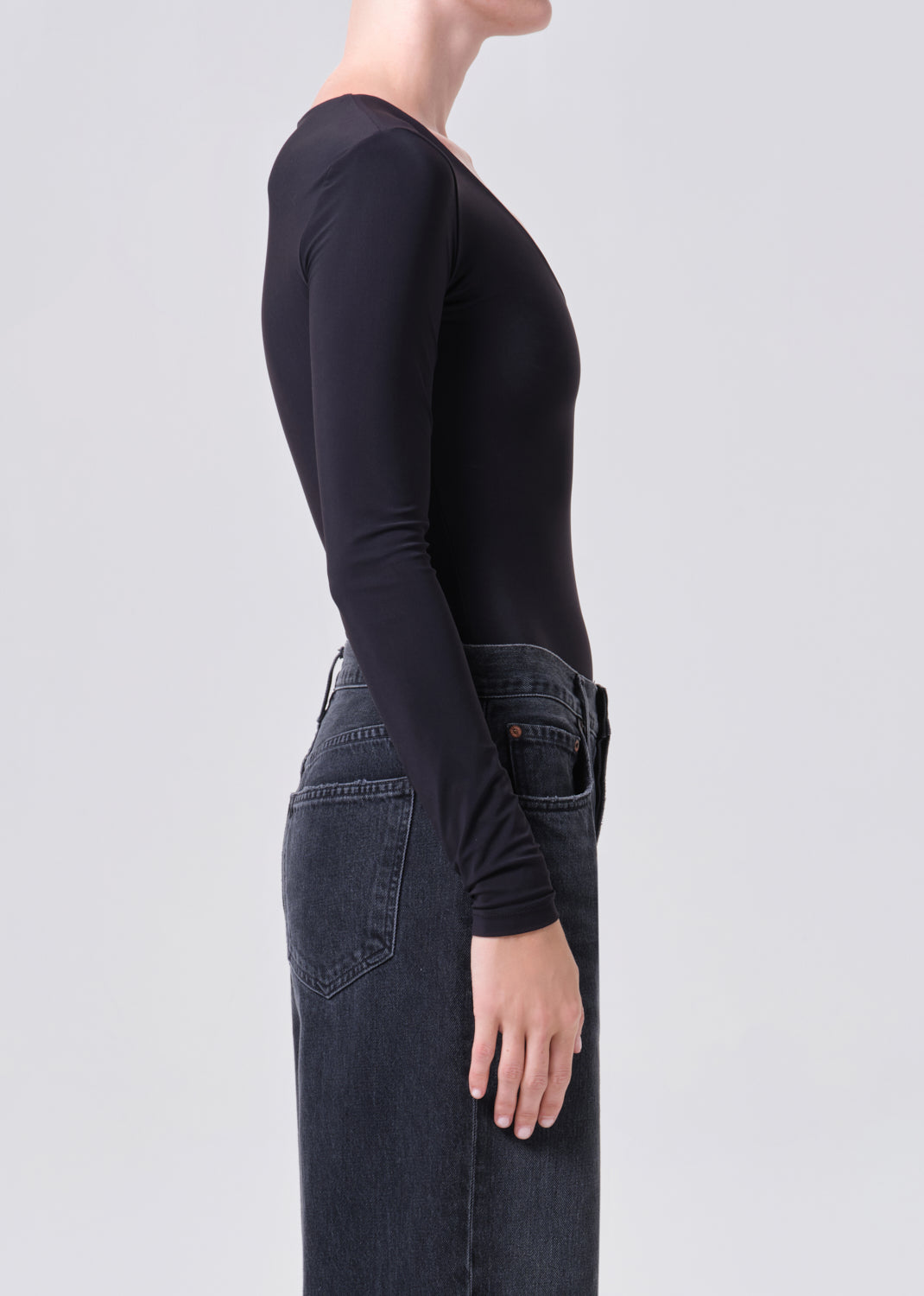 Person wearing a black long-sleeve top and dark jeans on a light gray background