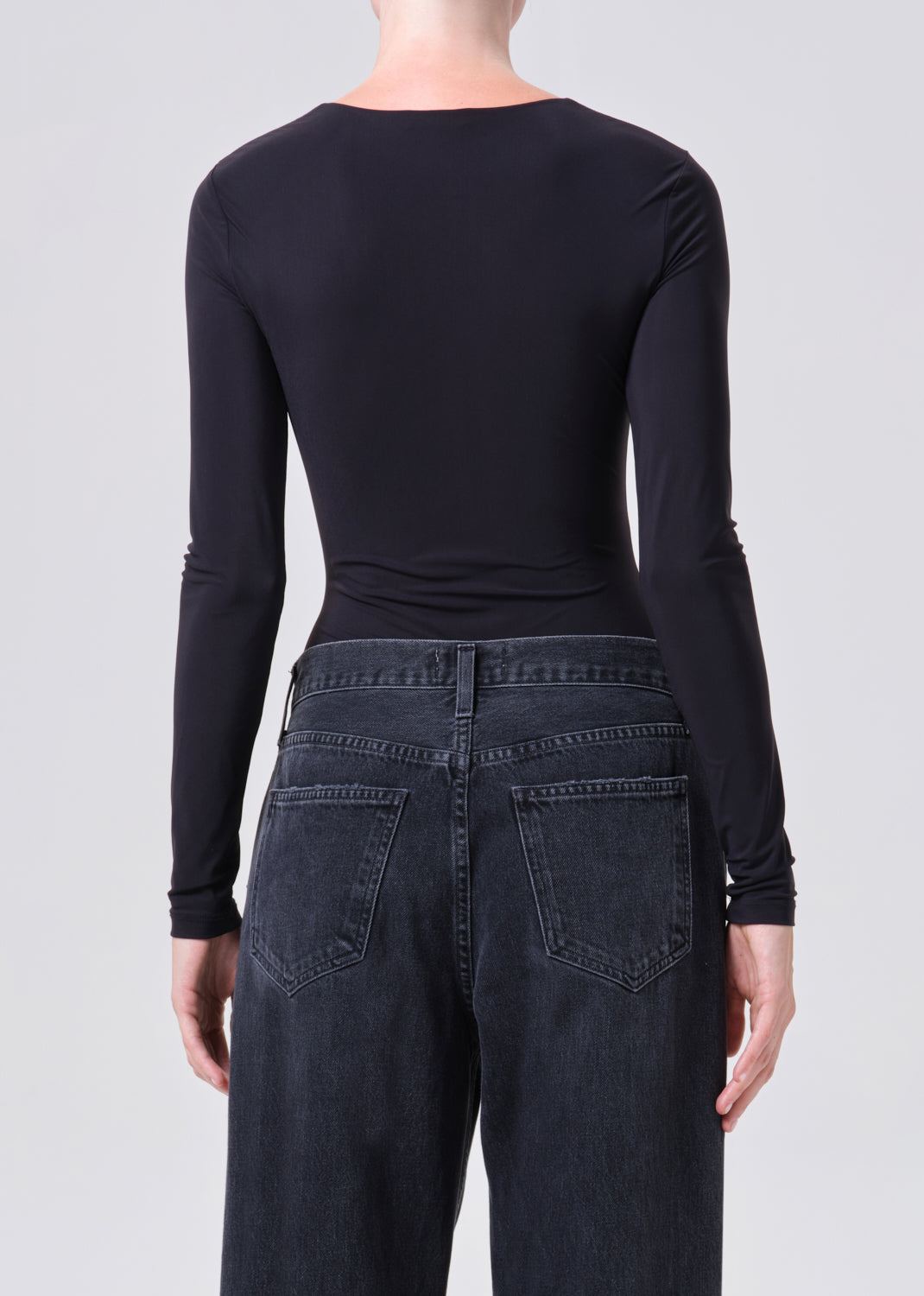 Person wearing a black long-sleeve top and dark jeans on a plain background
