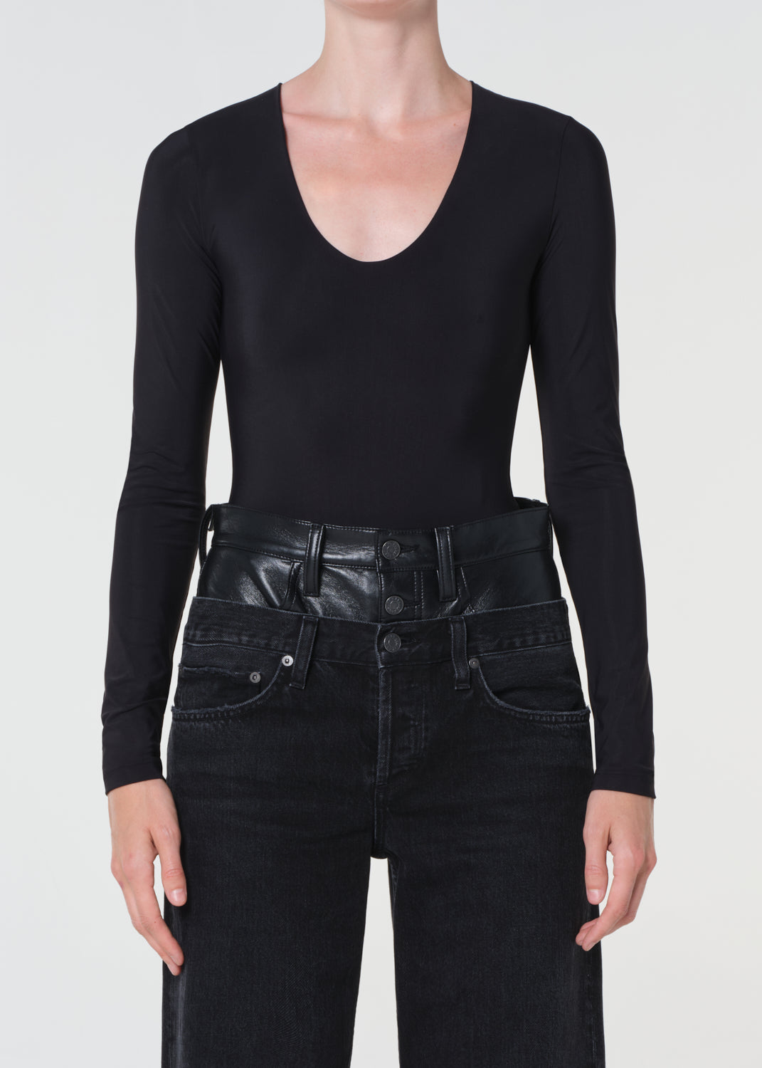Person wearing a black long-sleeve top and black leather pants on a white background