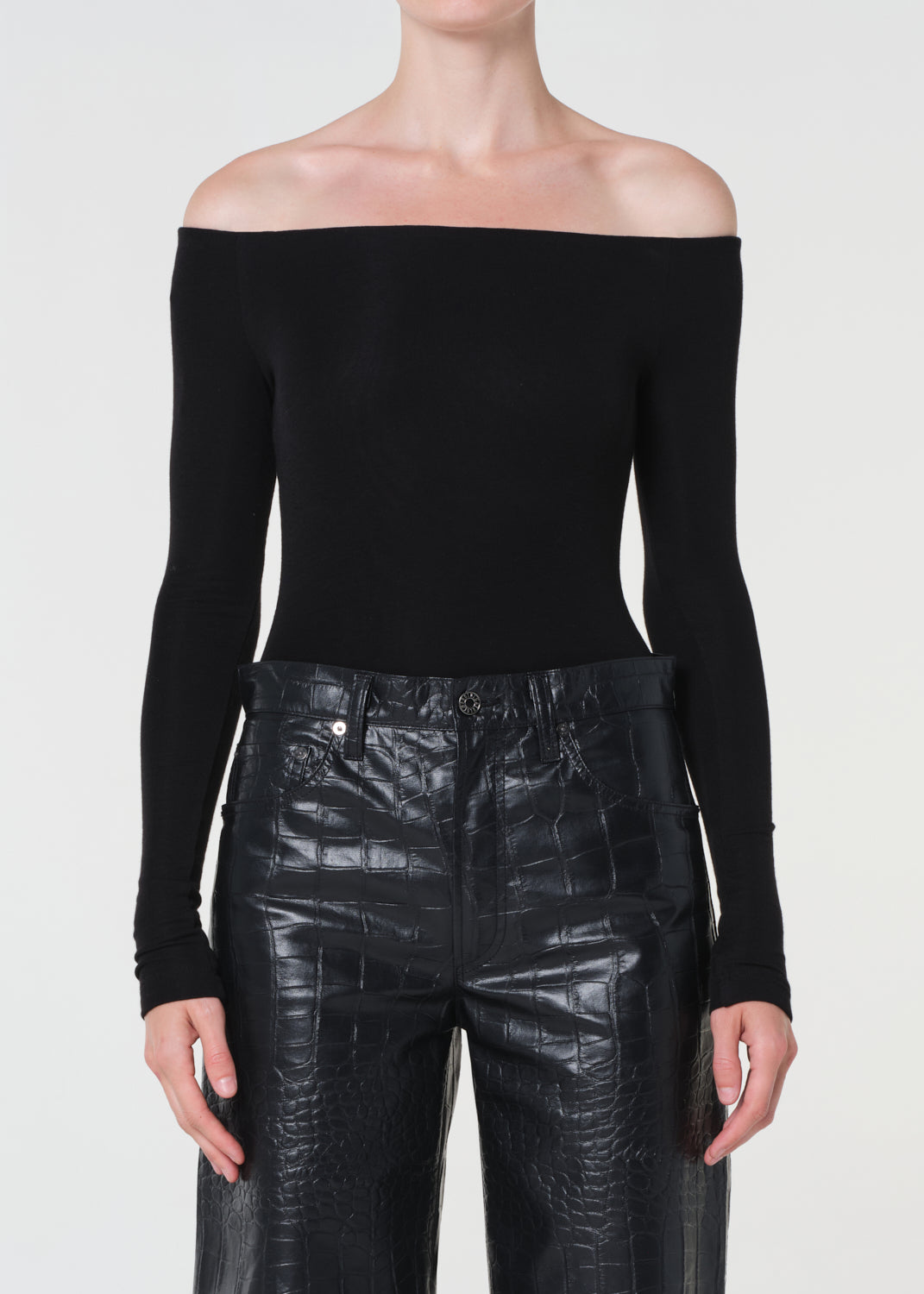 Person wearing a black off-shoulder top and black leather pants on a white background