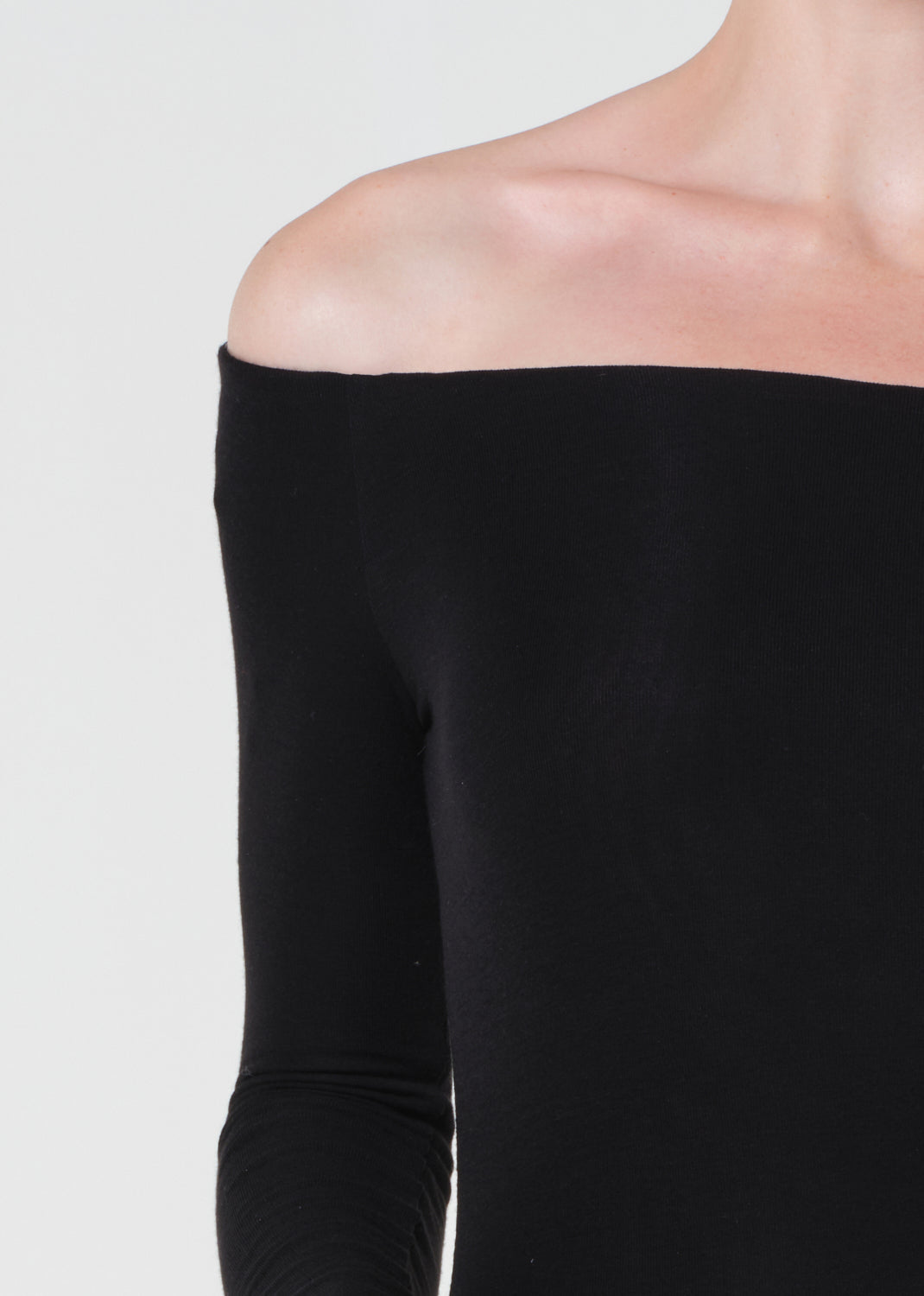 Black off-shoulder top worn by a person on a light gray background