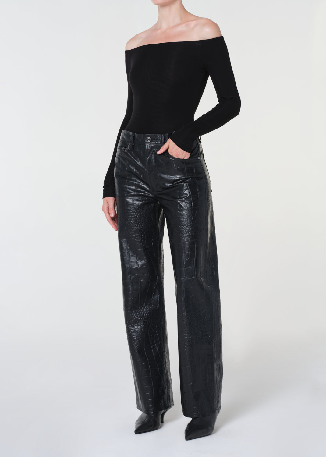 Person wearing a black off-shoulder top and shiny black pants on a white background