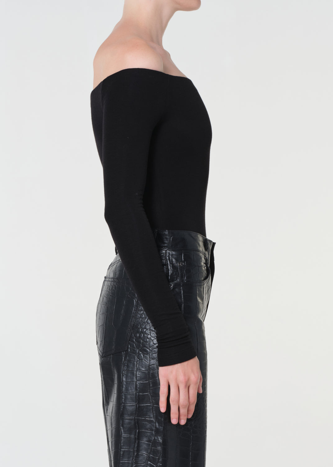 Person wearing a black off-shoulder top and black leather pants on a light gray background