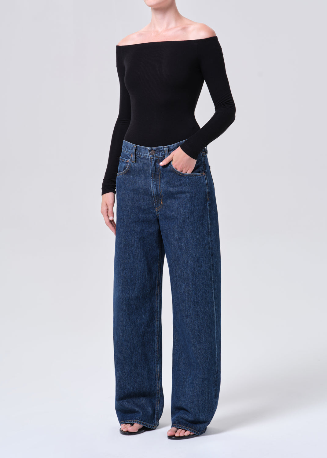 Person wearing a black off-shoulder top and blue jeans on a white background